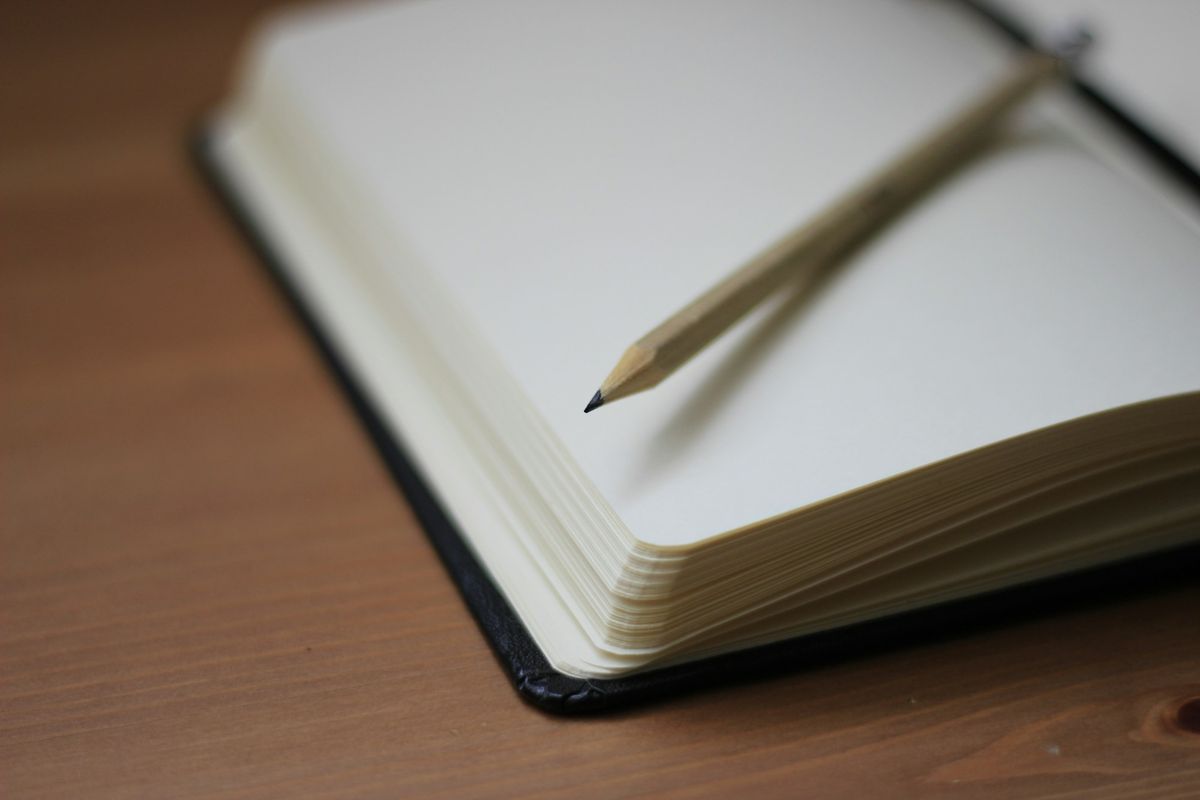 A pencil resting on an open notebook on a wooden desk